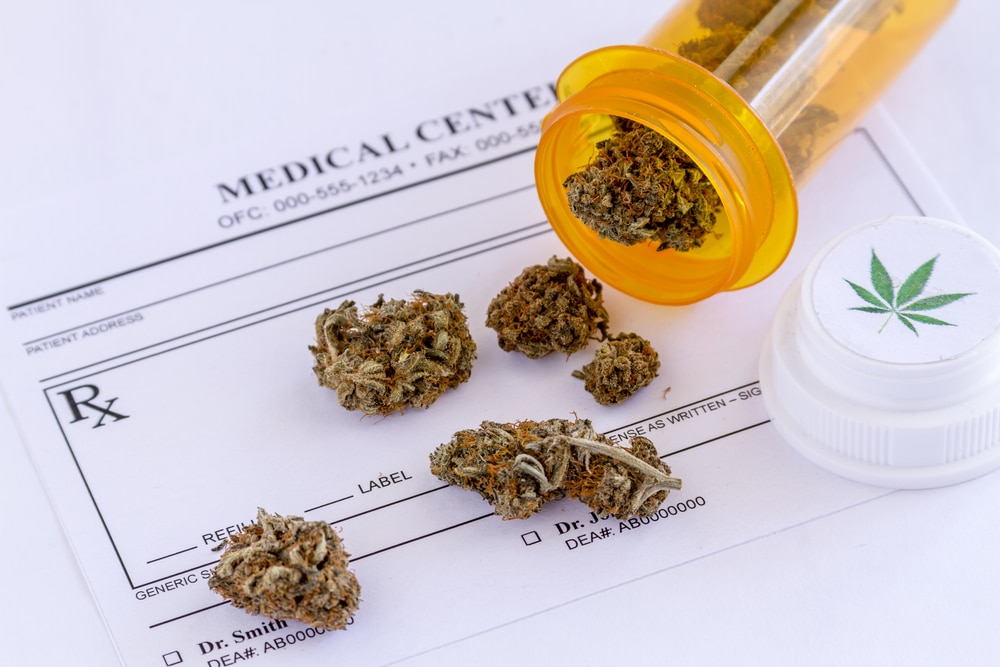 Medical marijuana buds spilling out of prescription bottle with lid onto blank medical prescription pad